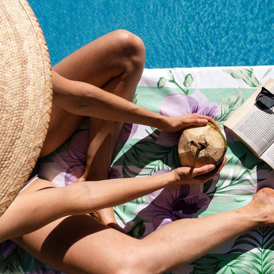 girl sitting by pool with book and coconut on floral towel